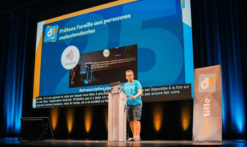 Conférence au Devfest Lille 2025 avec présentation d'une solution de sous-titrage en direct (ou vélotypie) pour les personnes sourdes et malentendantes, avec diapositive projetée en arrière-plan.
